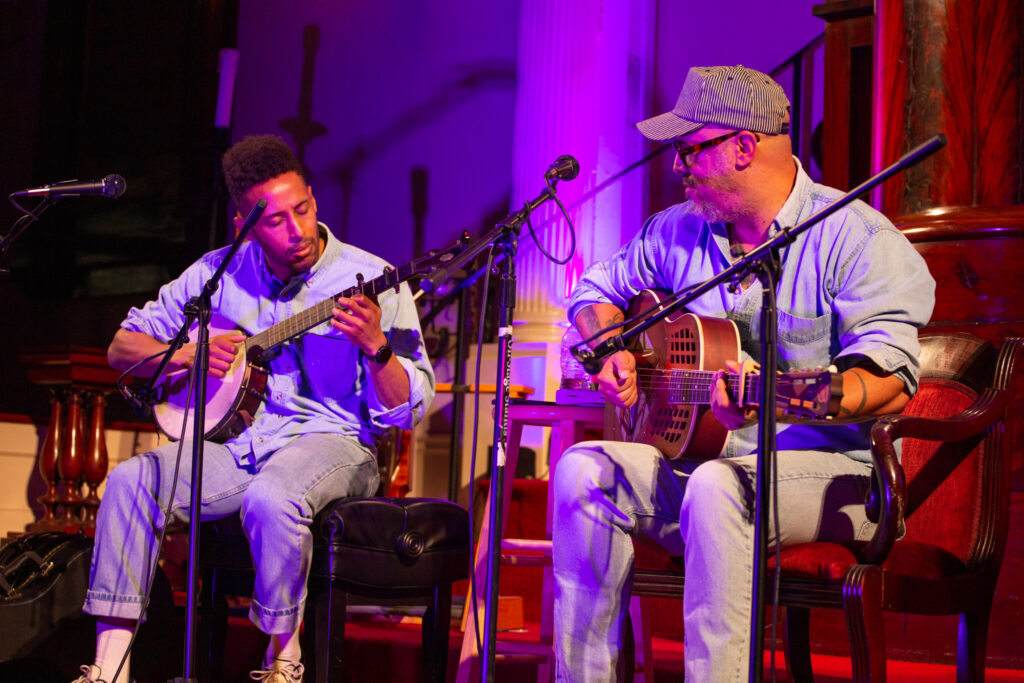 Photo of Michael Kebede playing banjo and Samuel James playing guitar