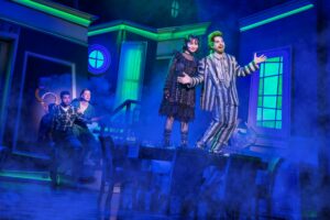 Photo from Beetlejuice of Lydia and Beetlejuice standing on a table.