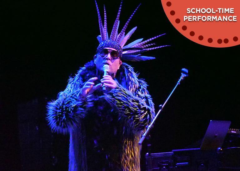 Photo of Firefly singing on stage wearing an Indigenous head dress, sunglasses and fur coat