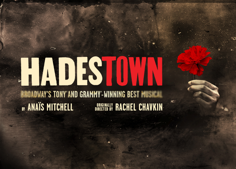 Graphic of Hadestown, the words are written in white and red, with a hand next to it holding a red carnation