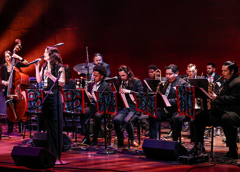 Photo of the members of Julia Keefe Indigenous Big Band sitting on stage, many with instruments, and one singing.