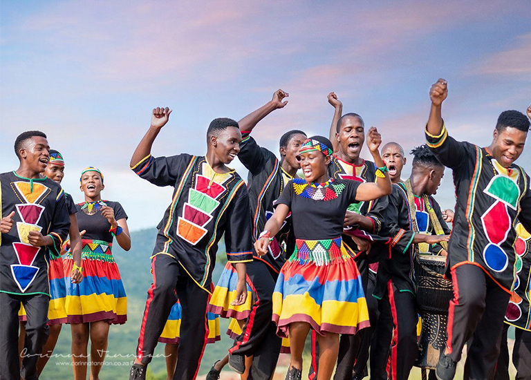 Photo of members of Ndlovu Youth Choir jumping around in colorful shirts and skirts while singing