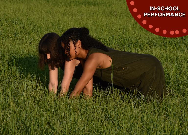 Photo of two dancers from little house dance, doing contemporary movement in a green field with long grass