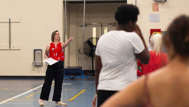 Liz Schildkret wearing a red blowse and black pants, pointing during an integrated arts learning game