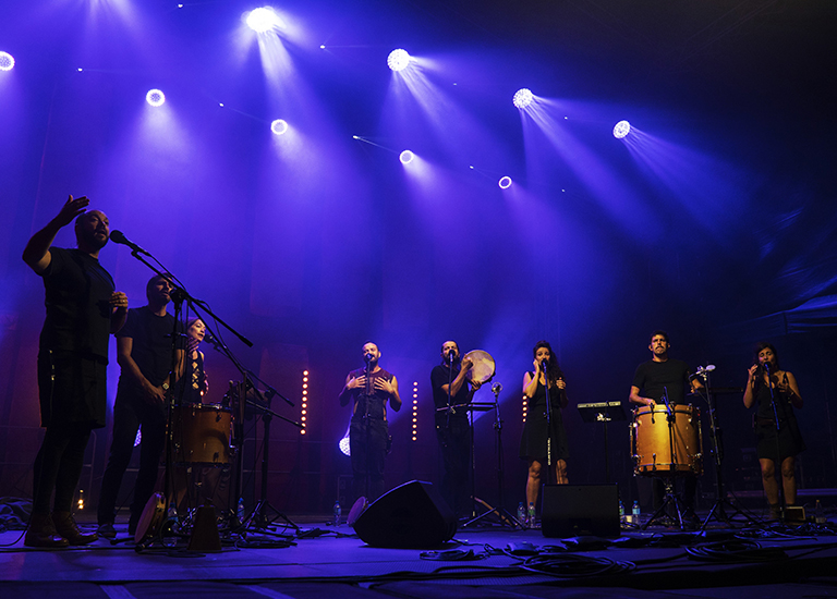 Photo of the seven members of the band Barrut on stage under blue light